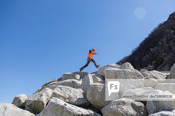 Worker jumping on stack of boulders at quarry