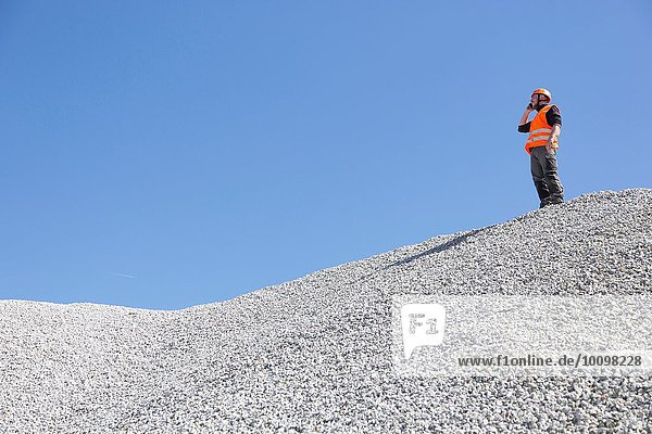 Quarry worker chatting on smartphone from quarry gravel mound