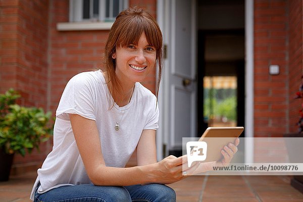 Mittlere erwachsene Frau  die im Freien sitzt und ein digitales Tablett hält.