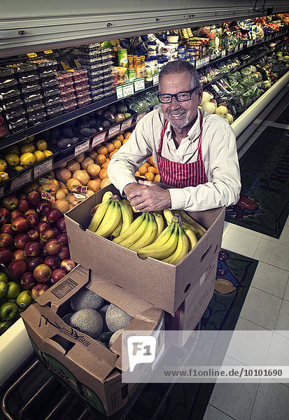 Ein Mann steht in einem Lebensmittelgeschäft neben einer Auslage mit frischem Obst und Gemüse.