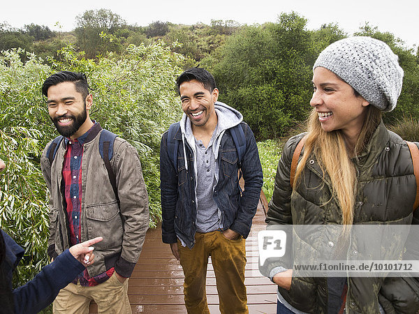 Smiling young woman and two young men walking in a park.