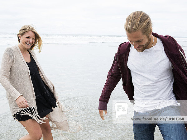 Young man and young woman walking on a beach  smiling.