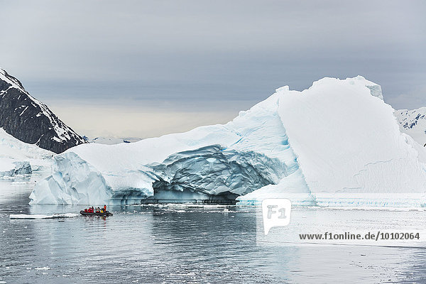 Gruppe von Menschen  die den Ozean in der Antarktis in einem Schlauchboot überqueren  im Hintergrund Eisberge.
