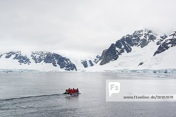 Group of people crossing the ocean in the Antarctic in a rubber boat  snow-covered mountains in the background.