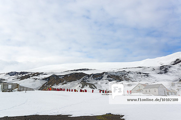 Group of people near a base on Deception Island  snow covered mountains in the background.