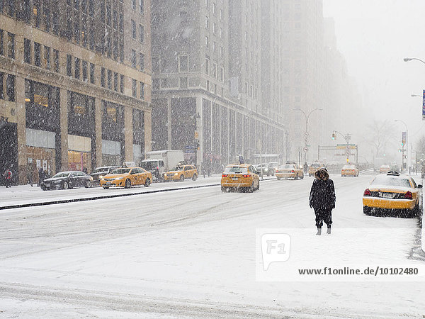 Mann  der während eines Schneesturms in einer Stadt im Schnee läuft  gelbe Taxis auf der Straße.