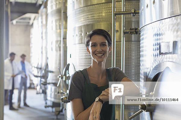 Portrait smiling vintner at stainless steel vat in winery cellar
