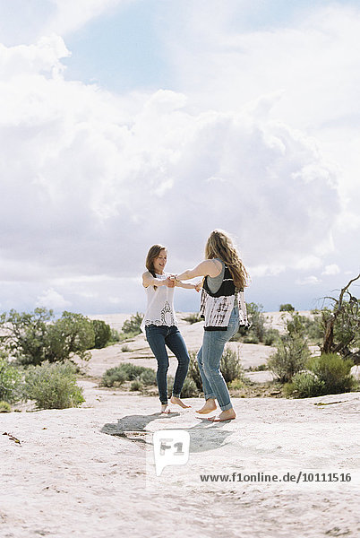 Two woman holding hands dancing in the desert.