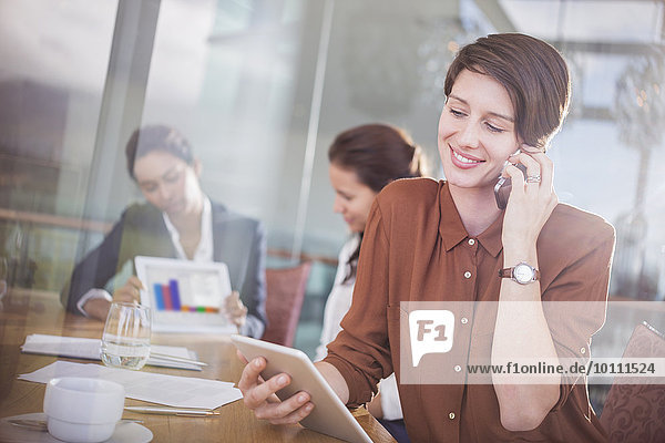Geschäftsfrau im Gespräch mit dem Handy und mit dem digitalen Tablett im Büro