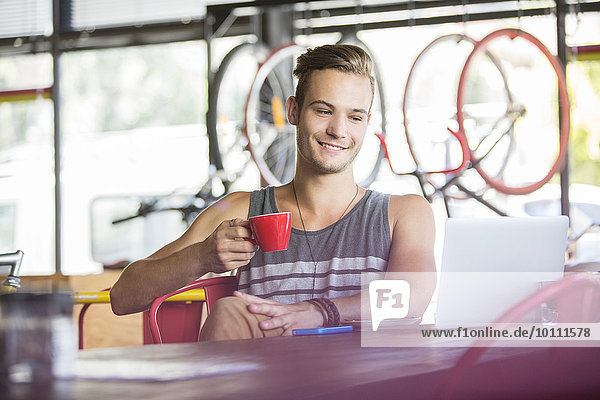 Smiling man drinking coffee at laptop in bike shop