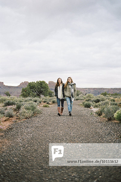 Two women walking side by side down a dirt road in a desert.