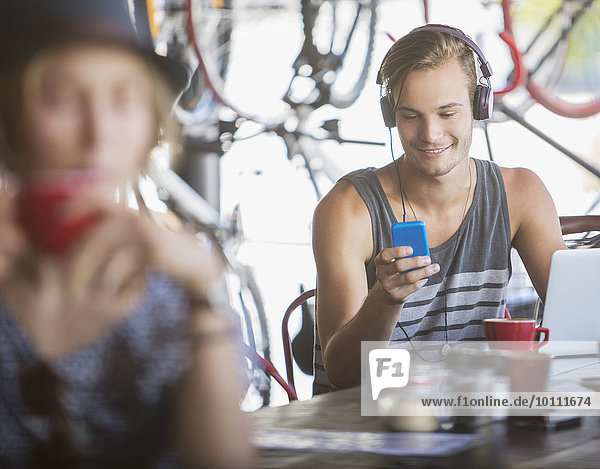 Junger Mann mit Kopfhörer und Laptop mit Handy im Cafe