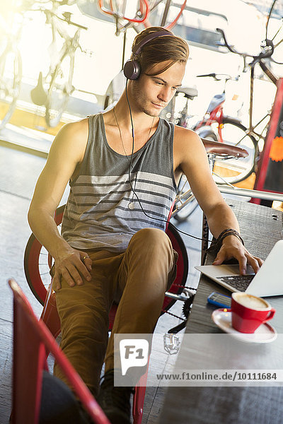 Mann mit Kopfhörer am Laptop im Cafe