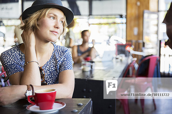 Nachdenkliche Frau mit Hut und Kaffee im Café