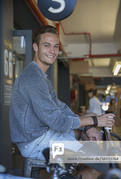 Portrait lächelnder junger Mann beim Kaffeetrinken im Café