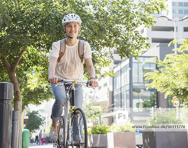 Portrait lächelnde junge Frau im Helm auf dem Fahrrad im Stadtpark