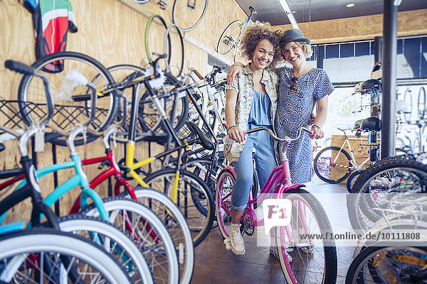 Portrait lächelnde Frauen beim Umarmen mit dem Fahrrad im Fahrradgeschäft