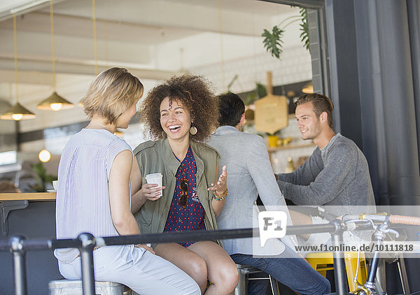 Lachende Freunde  die auf der Terrasse des Cafés Kaffee trinken.