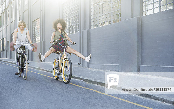 Playful women coasting on bicycles down urban street