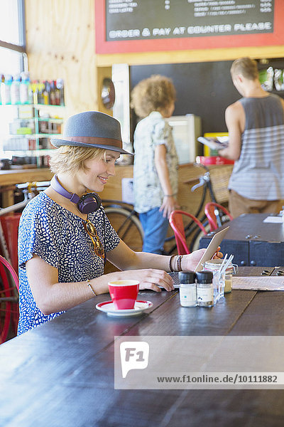 Frau im Hut mit digitalem Tablett im Café
