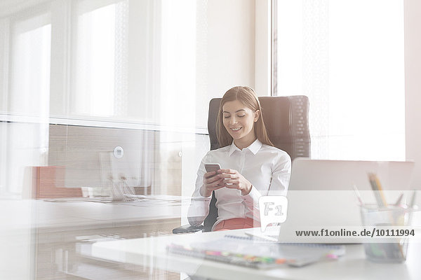 Geschäftsfrau SMS mit Handy im sonnigen Büro