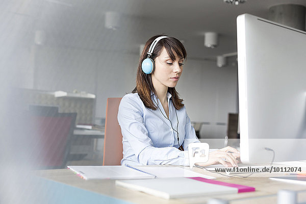 Brunette businesswoman with headphones working at computer in office