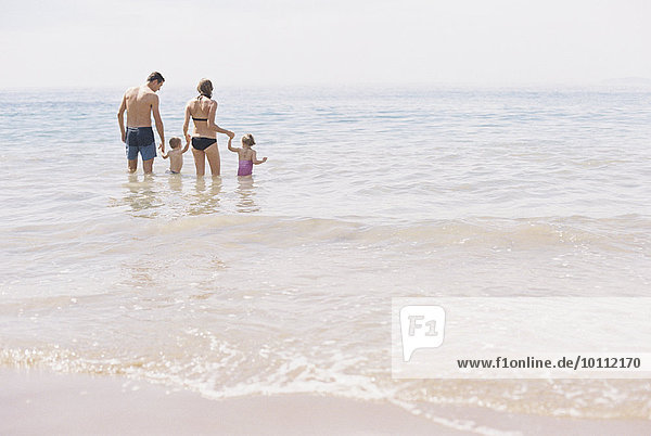 Couple with their son and daughter  A family standing in shallow water off the beach.