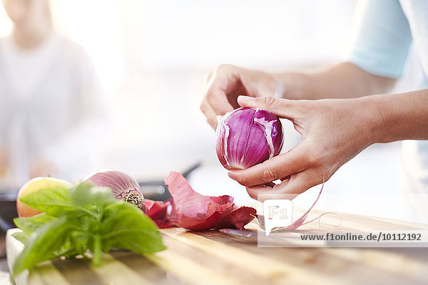 Woman peeling red onion in kitchen
