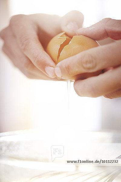 Close up woman cracking egg baking
