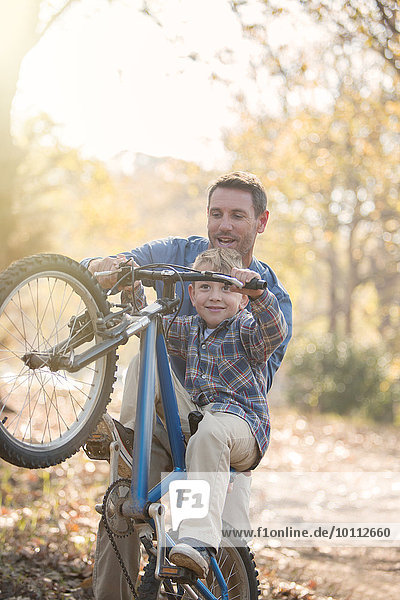 Father teaching son how to do a wheelie in woods