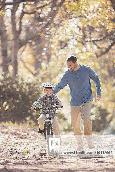 Father teaching son to ride a bicycle on path in woods