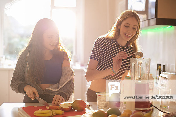 Teenage girls making smoothie in sunny kitchen