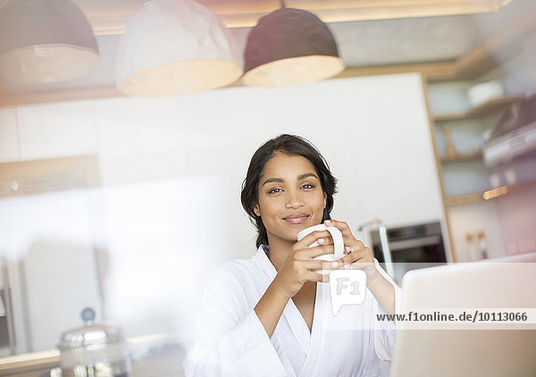 Portrait confident woman in bathrobe drinking coffee at laptop