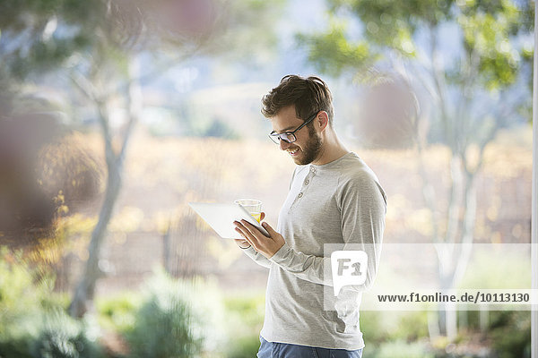 Man drinking orange juice and using digital tablet on patio