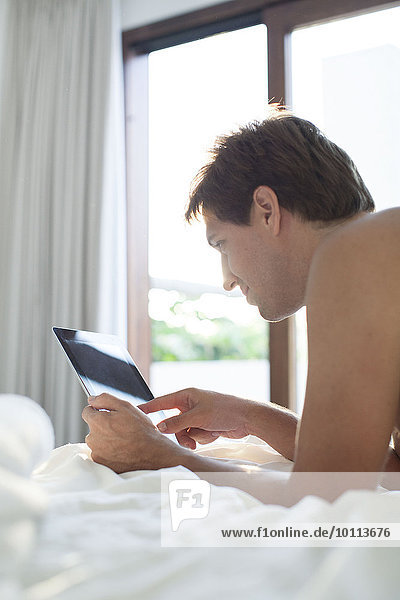 Mann im Bett liegend mit digitalem Tablett