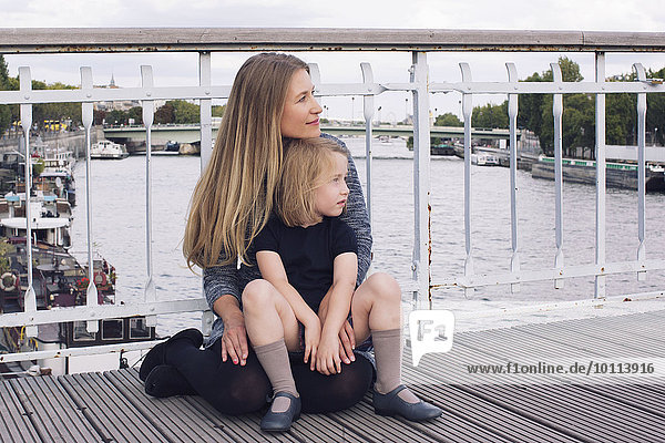 Mutter und Tochter sitzen zusammen auf der Brücke über den Kanal.