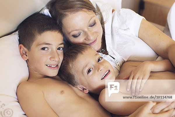 Mutter und kleine Söhne entspannen gemeinsam auf dem Bett  Porträt