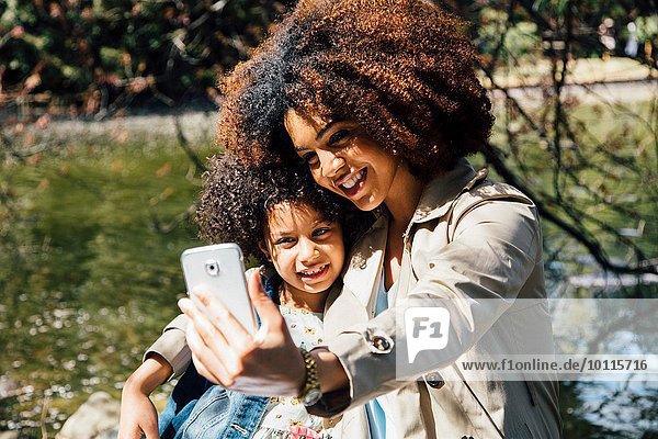 Mutter mit Arm um Tochter mit Smartphone  um Selfie zu nehmen