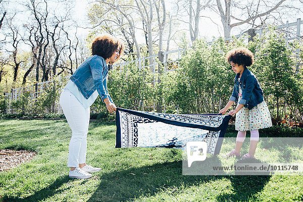 Seitenansicht von Mutter und Tochter beim Auslegen der Decke auf Rasen