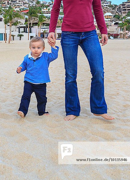 Mother and son on beach  holding hands  low section