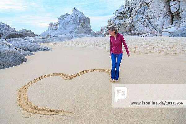 Mid adult woman on beach  drawing heart shape with feet