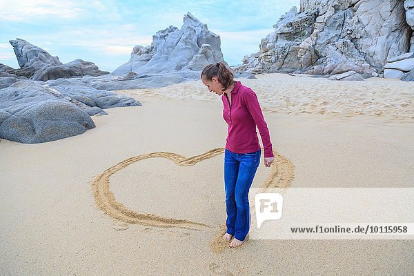 Mid adult woman on beach  drawing heart shape with feet