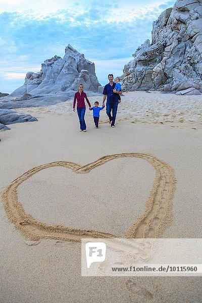 Young family walking on beach  heart shape in foreground
