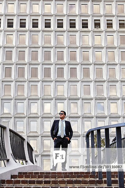 Business man standing at the top of stairway  wearing sunglasses  hands in pockets  looking away