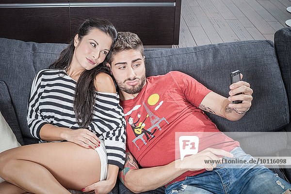 Young couple taking smartphone selfie on sofa