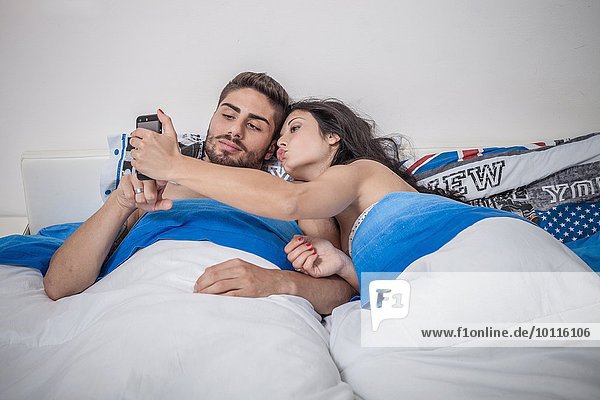 Young couple taking smartphone selfie in bed