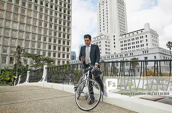 Geschäftsmann auf erhöhtem Gehweg mit Fahrrad auf Smartphone  Los Angeles City Hall  Kalifornien  USA