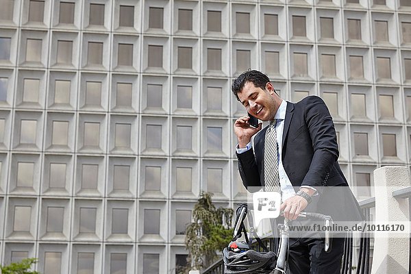 Mid adult business man holding bicycle  making telephone call using smartphone