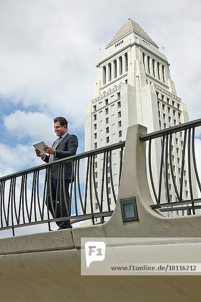 Geschäftsmann auf dem Gehweg stehend mit Blick auf das digitale Tablett  Los Angeles City Hall  Kalifornien  USA