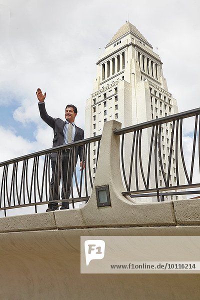 Geschäftsmann auf dem Gehweg stehend  winkend  lächelnd  Los Angeles City Hall  Kalifornien  USA